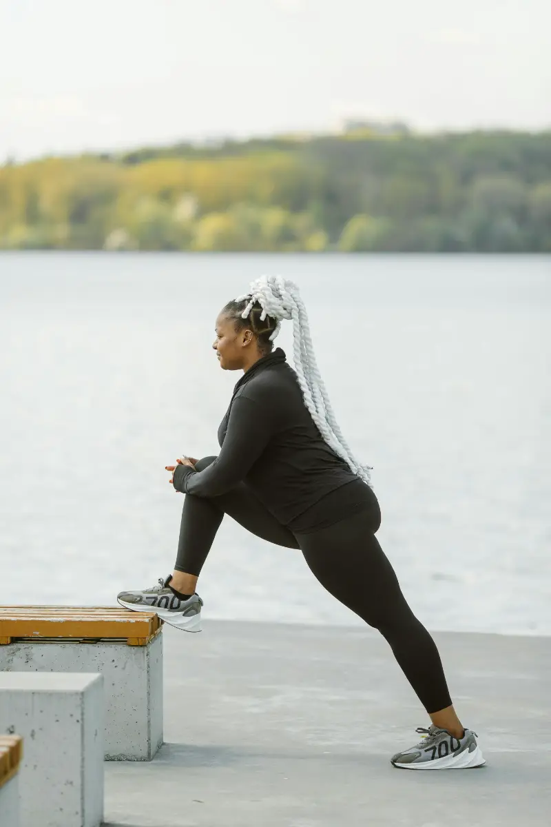 Plus-size woman in active wear stretching outdoors by a lake, embracing fitness and health.